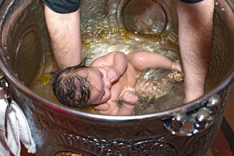Infant's feet ascending from baptismal font water during baptising in Greece photographer