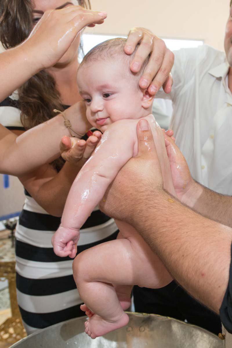 Infant's feet ascending from baptismal font water during baptising in Greece photographer