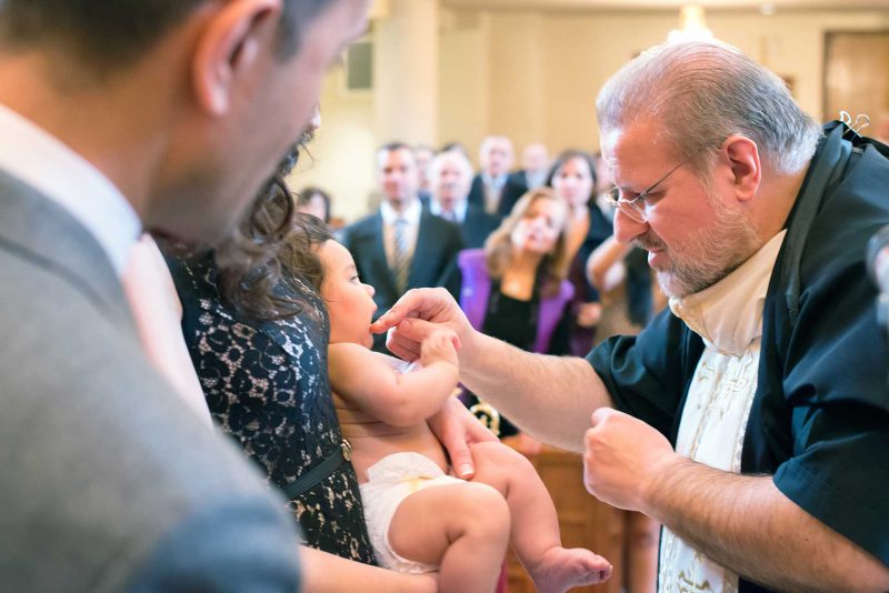 Infant's feet ascending from baptismal font water during baptising in Greece photographer