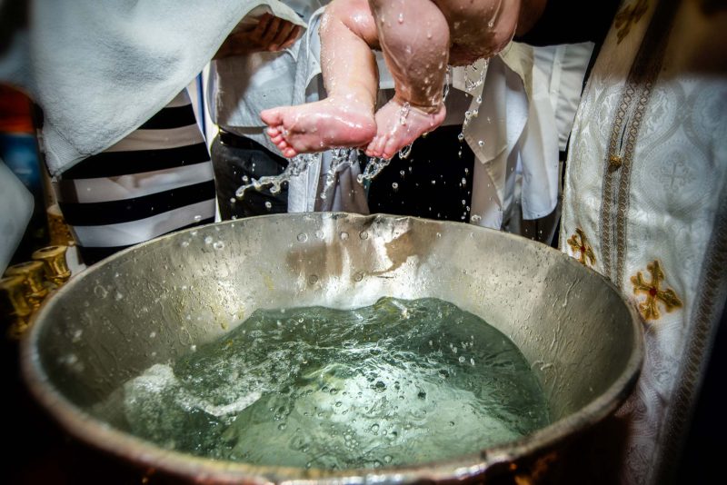 Infant's feet ascending from baptismal font water during baptising in Greece photographer